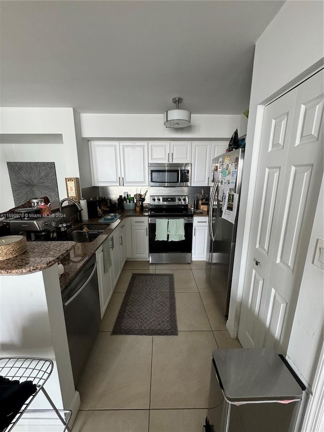 kitchen with stainless steel appliances, white cabinets, kitchen peninsula, sink, and light tile patterned floors