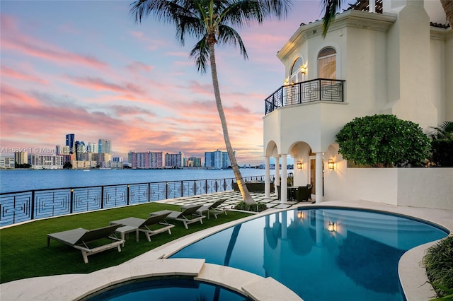 pool at dusk with a water view and an in ground hot tub