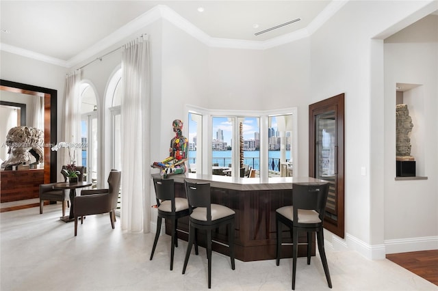 bar with a water view, light hardwood / wood-style floors, and ornamental molding