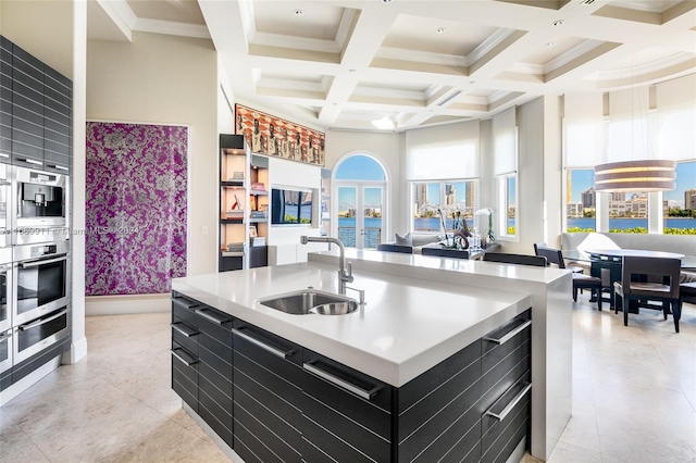 kitchen with coffered ceiling, sink, a center island with sink, beamed ceiling, and a high ceiling