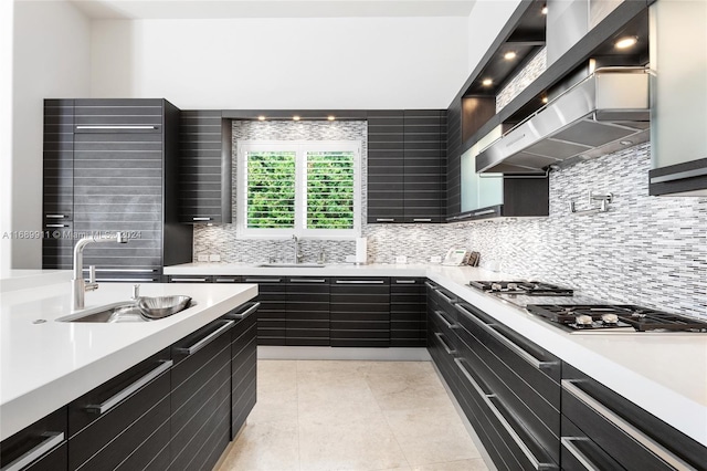 kitchen with wall chimney exhaust hood, decorative backsplash, sink, and stainless steel gas cooktop