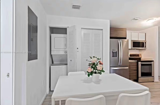 kitchen with stacked washing maching and dryer, a breakfast bar area, light hardwood / wood-style flooring, and appliances with stainless steel finishes