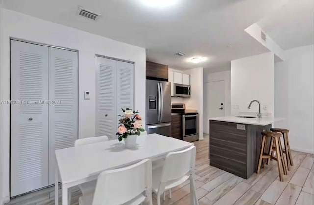 kitchen featuring kitchen peninsula, appliances with stainless steel finishes, dark brown cabinetry, and light hardwood / wood-style flooring