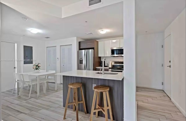 kitchen with stainless steel appliances, white cabinetry, sink, light hardwood / wood-style floors, and a breakfast bar area