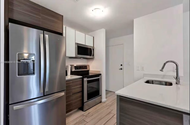 kitchen with stainless steel appliances, white cabinetry, sink, dark brown cabinets, and light hardwood / wood-style flooring