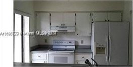 kitchen featuring ventilation hood, white appliances, and white cabinets