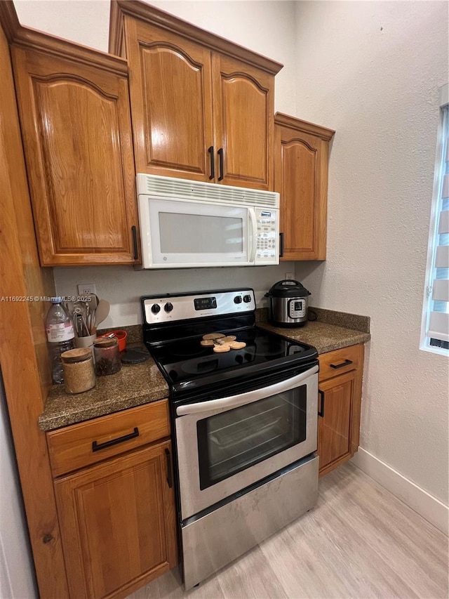 kitchen featuring dark stone countertops, light hardwood / wood-style floors, and stainless steel electric stove