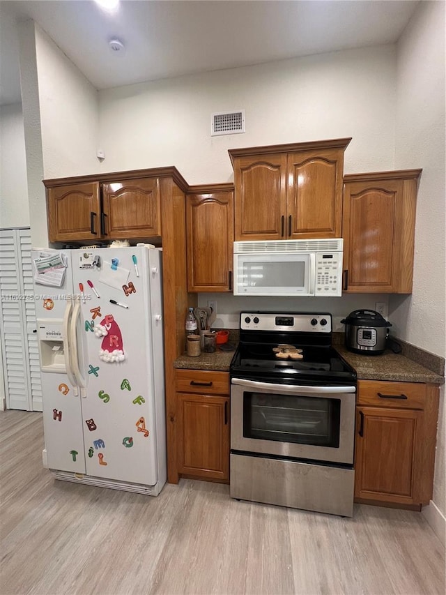 kitchen with white appliances, light hardwood / wood-style flooring, and dark stone countertops