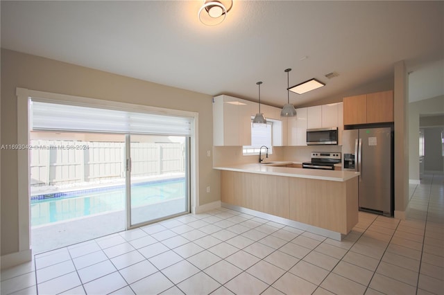 kitchen featuring kitchen peninsula, decorative light fixtures, vaulted ceiling, light brown cabinetry, and appliances with stainless steel finishes