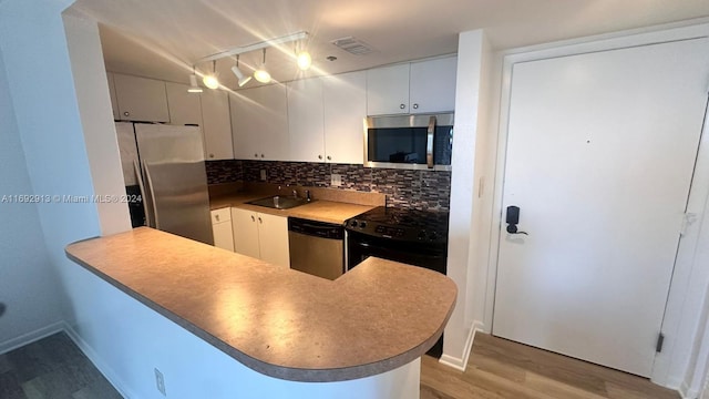 kitchen with light hardwood / wood-style floors, kitchen peninsula, appliances with stainless steel finishes, white cabinets, and decorative backsplash