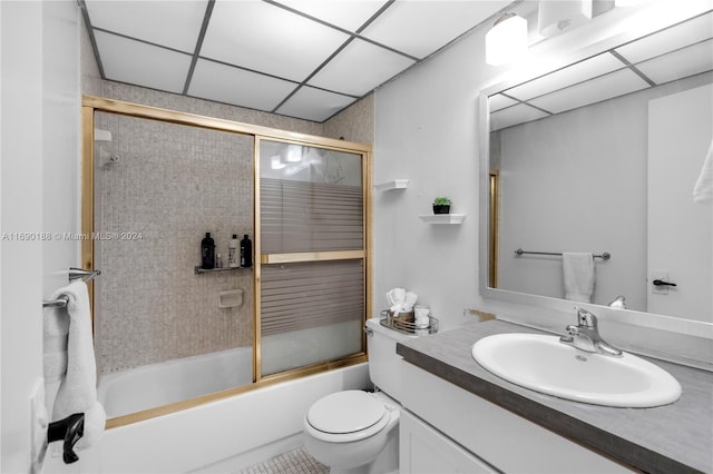 full bathroom with a drop ceiling, combined bath / shower with glass door, vanity, tile patterned floors, and toilet