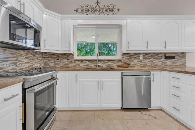 kitchen featuring sink, appliances with stainless steel finishes, white cabinetry, decorative backsplash, and dark stone counters