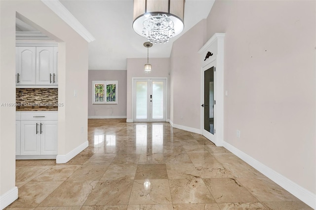 entryway with french doors, ornamental molding, and an inviting chandelier