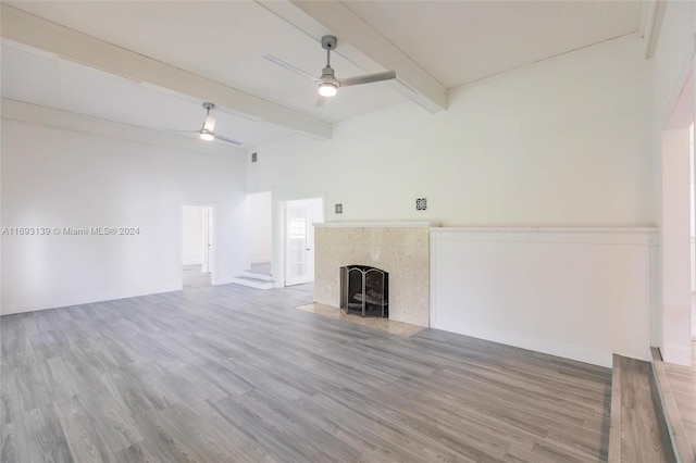 unfurnished living room featuring hardwood / wood-style floors, a tiled fireplace, beam ceiling, and ceiling fan