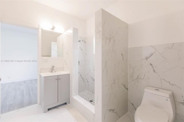 bathroom with tile walls, tiled shower, toilet, and vanity