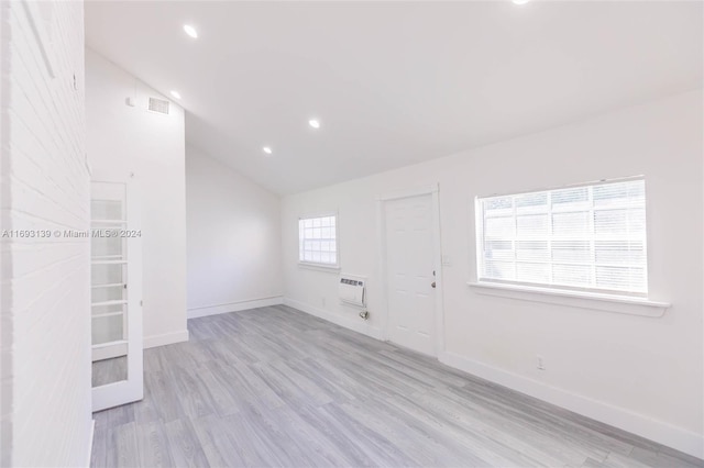 empty room featuring light wood-type flooring, a wall unit AC, and high vaulted ceiling