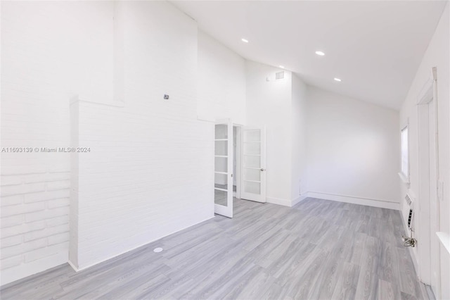 spare room with light hardwood / wood-style floors, brick wall, and high vaulted ceiling