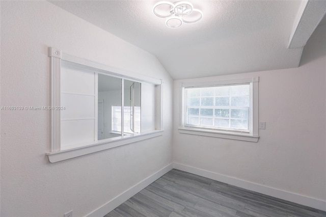 spare room featuring a textured ceiling, vaulted ceiling, and wood-type flooring