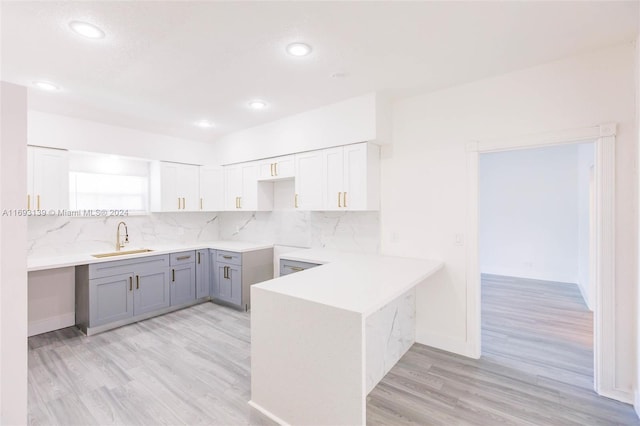 kitchen featuring decorative backsplash, light hardwood / wood-style floors, kitchen peninsula, and sink