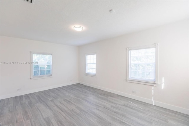 empty room with a wealth of natural light, a textured ceiling, and light wood-type flooring