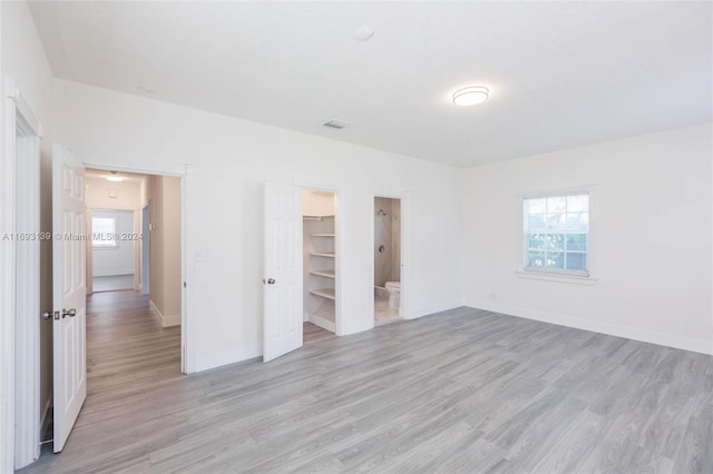 unfurnished bedroom featuring connected bathroom, a closet, light wood-type flooring, and a walk in closet