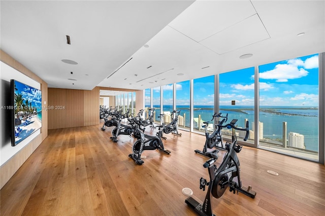 gym featuring expansive windows, light wood-type flooring, and a water view