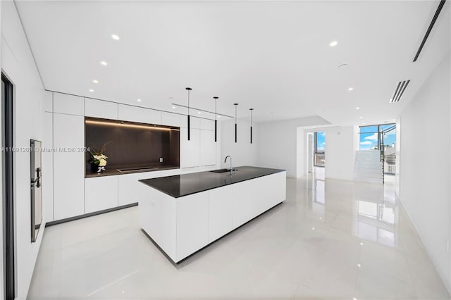 kitchen with light tile patterned flooring, decorative light fixtures, sink, white cabinets, and a spacious island