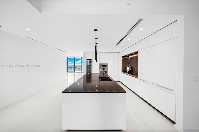 kitchen featuring white cabinetry, sink, hanging light fixtures, stainless steel double oven, and an island with sink