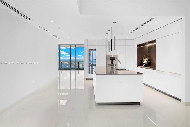 kitchen featuring white cabinets, hanging light fixtures, sink, and an island with sink