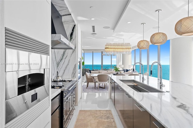 kitchen with stainless steel appliances, decorative light fixtures, light stone countertops, an inviting chandelier, and a water view