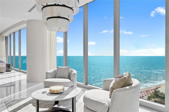 sunroom / solarium with a view of the beach, a water view, and an inviting chandelier