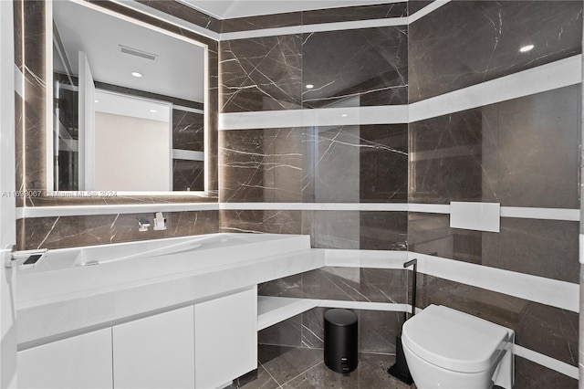 bathroom with vanity, toilet, and tile walls