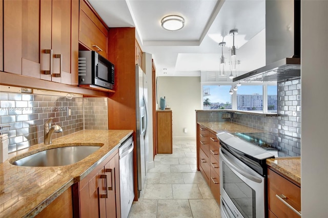 kitchen with light stone counters, sink, wall chimney range hood, appliances with stainless steel finishes, and decorative light fixtures