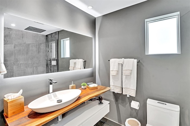 bathroom with a tile shower, plenty of natural light, vanity, and toilet