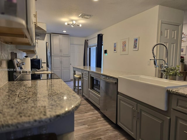 kitchen with appliances with stainless steel finishes, gray cabinets, light stone countertops, hardwood / wood-style floors, and sink