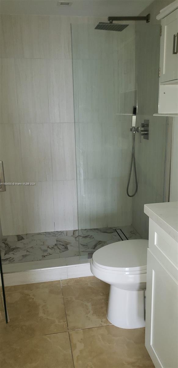 bathroom with tile patterned floors, vanity, toilet, and tiled shower