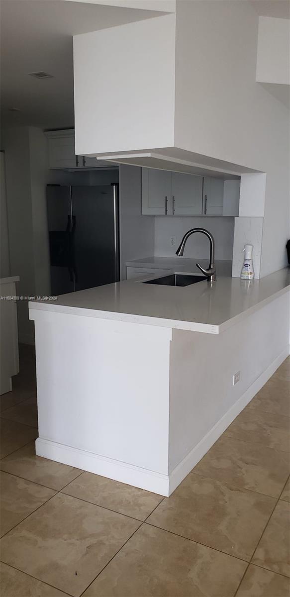 kitchen with kitchen peninsula, light tile patterned floors, sink, and stainless steel fridge