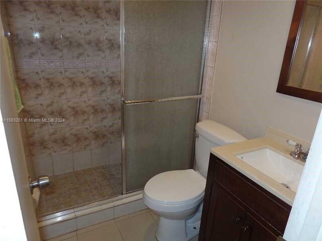 bathroom featuring toilet, vanity, tile patterned floors, and a shower with door