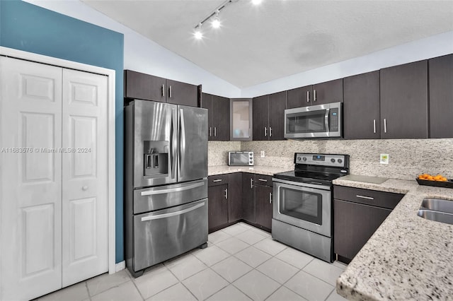 kitchen featuring stainless steel appliances, light stone counters, backsplash, lofted ceiling, and dark brown cabinets