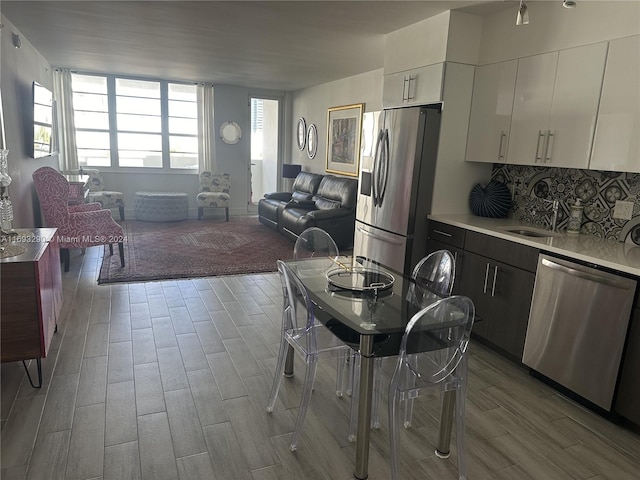 kitchen with appliances with stainless steel finishes, decorative backsplash, sink, white cabinets, and light hardwood / wood-style flooring