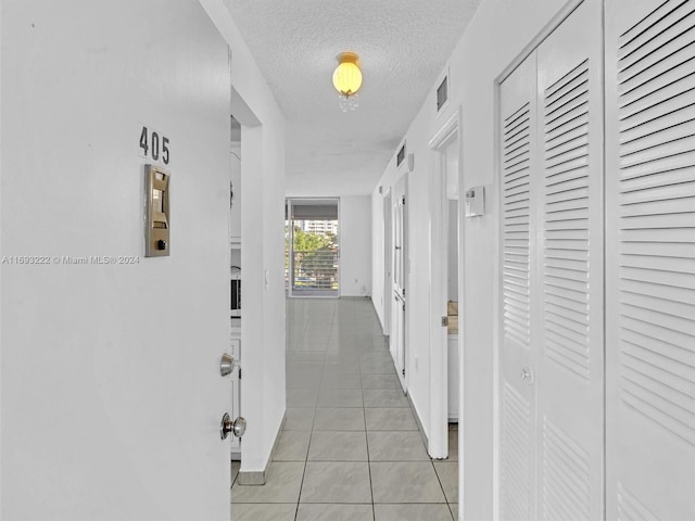 hallway with a textured ceiling and light tile patterned flooring