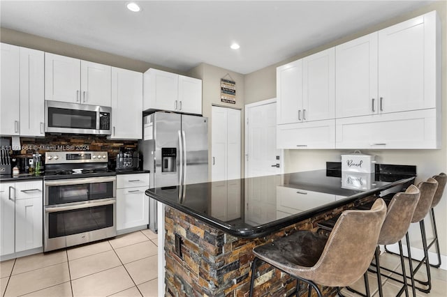 kitchen featuring stainless steel appliances, light tile patterned flooring, white cabinetry, kitchen peninsula, and a kitchen breakfast bar