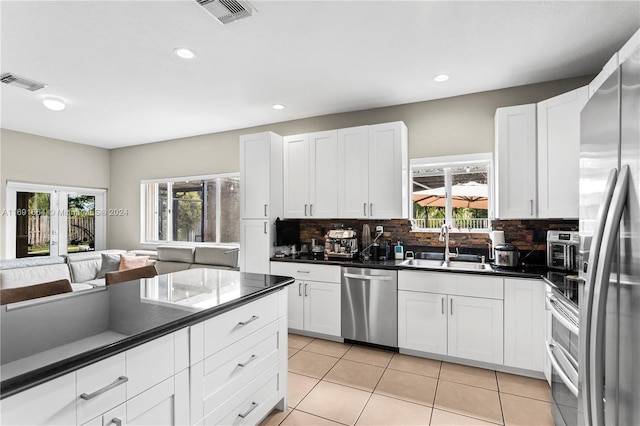 kitchen featuring tasteful backsplash, appliances with stainless steel finishes, light tile patterned floors, sink, and white cabinets