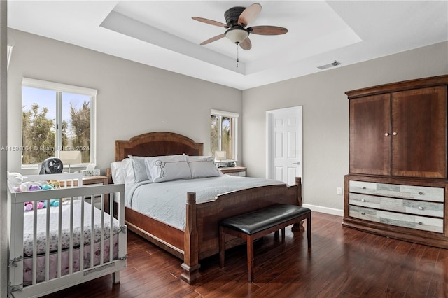 bedroom with ceiling fan, dark hardwood / wood-style floors, and a tray ceiling