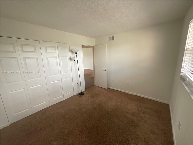 unfurnished bedroom featuring a closet, dark carpet, and a textured ceiling