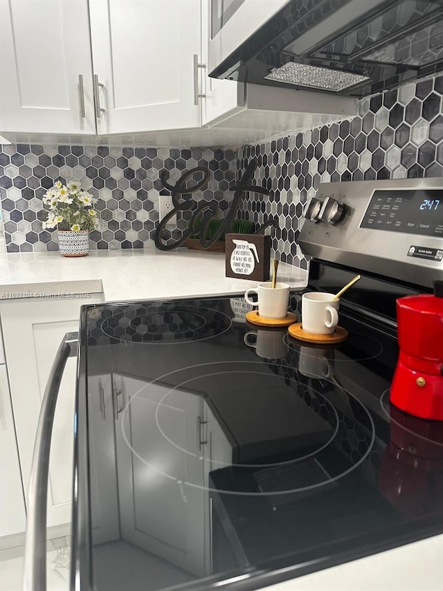 interior details with tasteful backsplash, electric range, and white cabinets