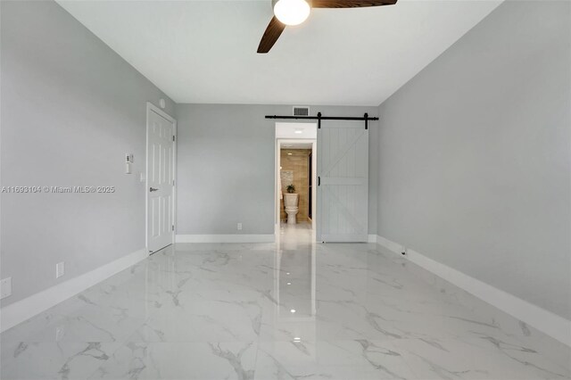 unfurnished bedroom featuring marble finish floor, baseboards, a ceiling fan, and a barn door