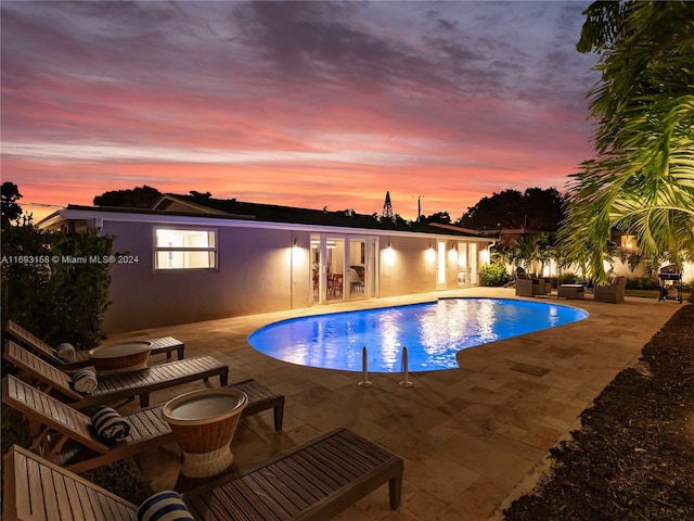 pool at dusk featuring french doors, a patio, and an outdoor living space