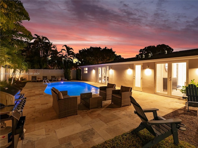 pool at dusk with french doors, area for grilling, and a patio area