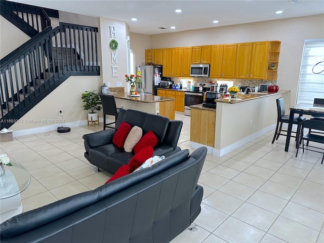 kitchen featuring kitchen peninsula, light tile patterned flooring, backsplash, appliances with stainless steel finishes, and dark stone countertops